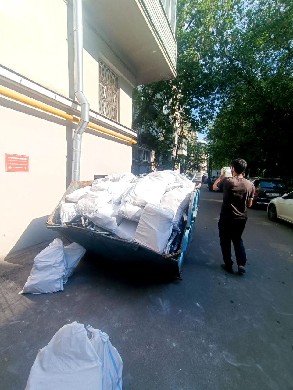 Грузчик несёт мешок к контейнеру